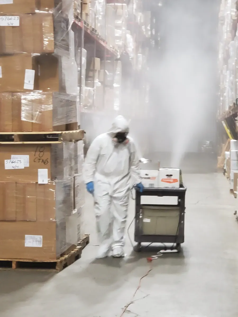 A Marrone technician in a protective suit fogging a warehouse aisle